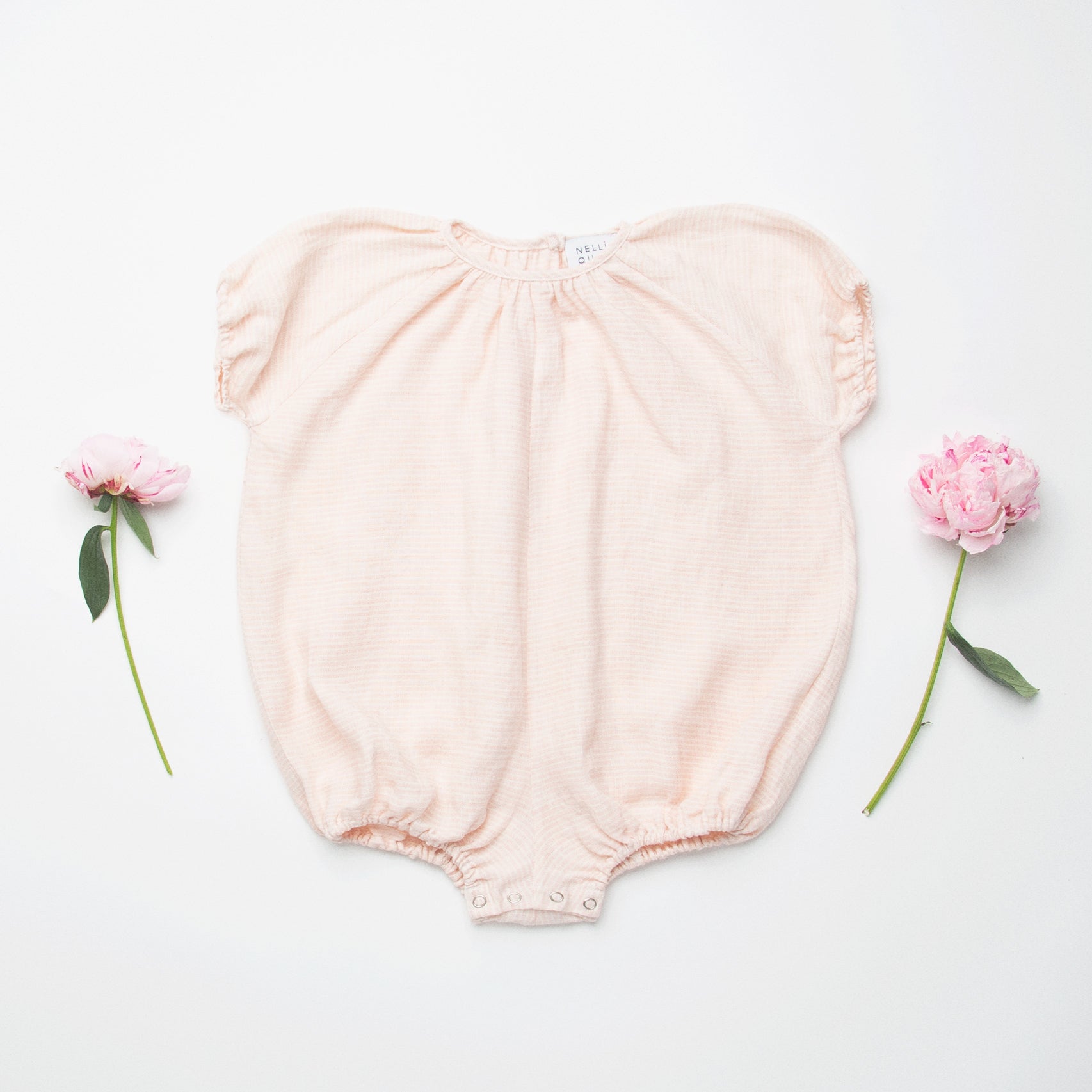 All in one romper, with short puffed elasticated sleeves and gathered neck to create a full, loose body shape. Closes at the back with single mother of pearl button, has elasticated leg holes and poppers for ease of opening. Designed to sit at the top of the thigh, perfect layered over tights in cooler weather and without in the summer. Made from super soft pale pink stripe linen.