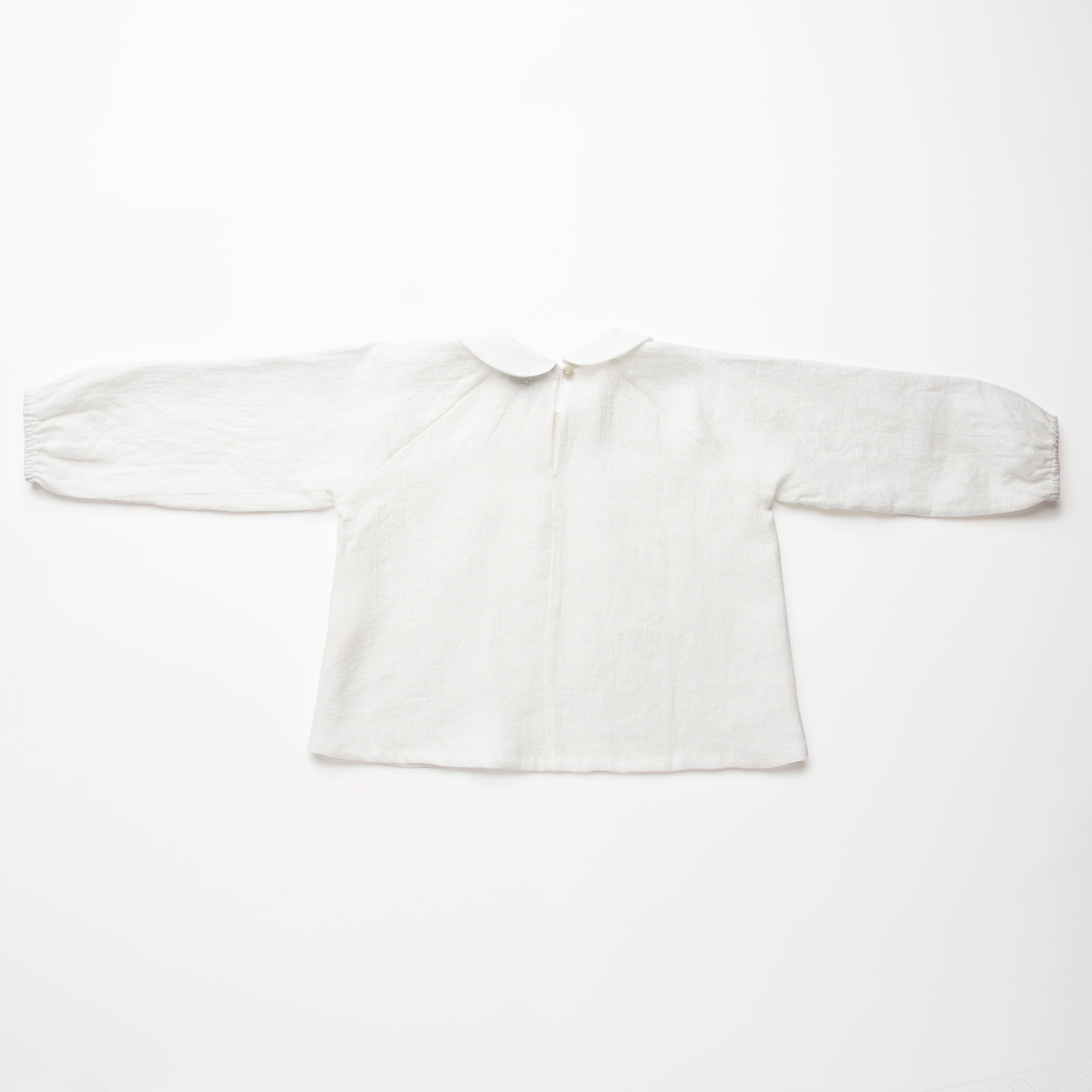 Loose fit, raglan sleeve white Linen blouse, with long elasticated sleeves, Peter Pan collar and single mother of pearl button at the back of the neck.  