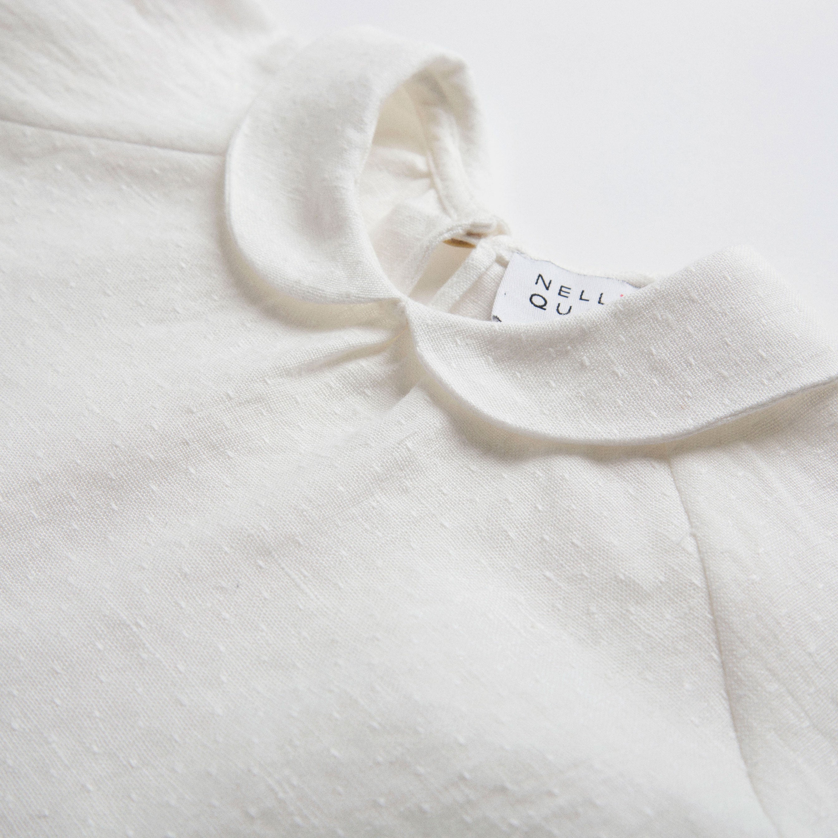 Loose fit, raglan sleeve white Linen blouse, with long elasticated sleeves, Peter Pan collar and single mother of pearl button at the back of the neck. 