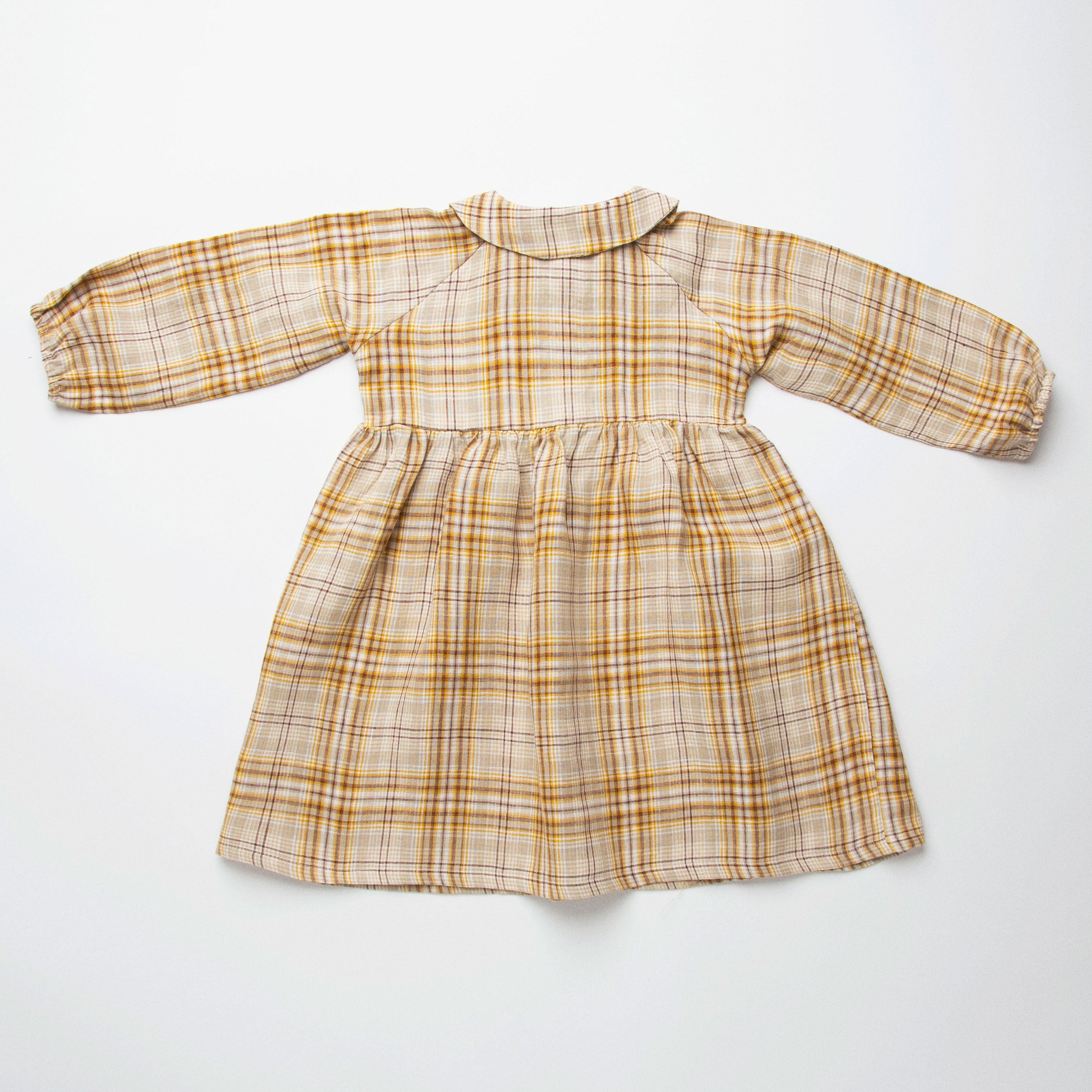 Long sleeve raglan dress with empire line, elasticated cuffs, Peter Pan collar and wooden button up front. Attached gathered skirt sits at a slightly longer length below the knee. Designed to be oversized for a stylish, comfortable fit. Made from a buttermilk plaid linen.