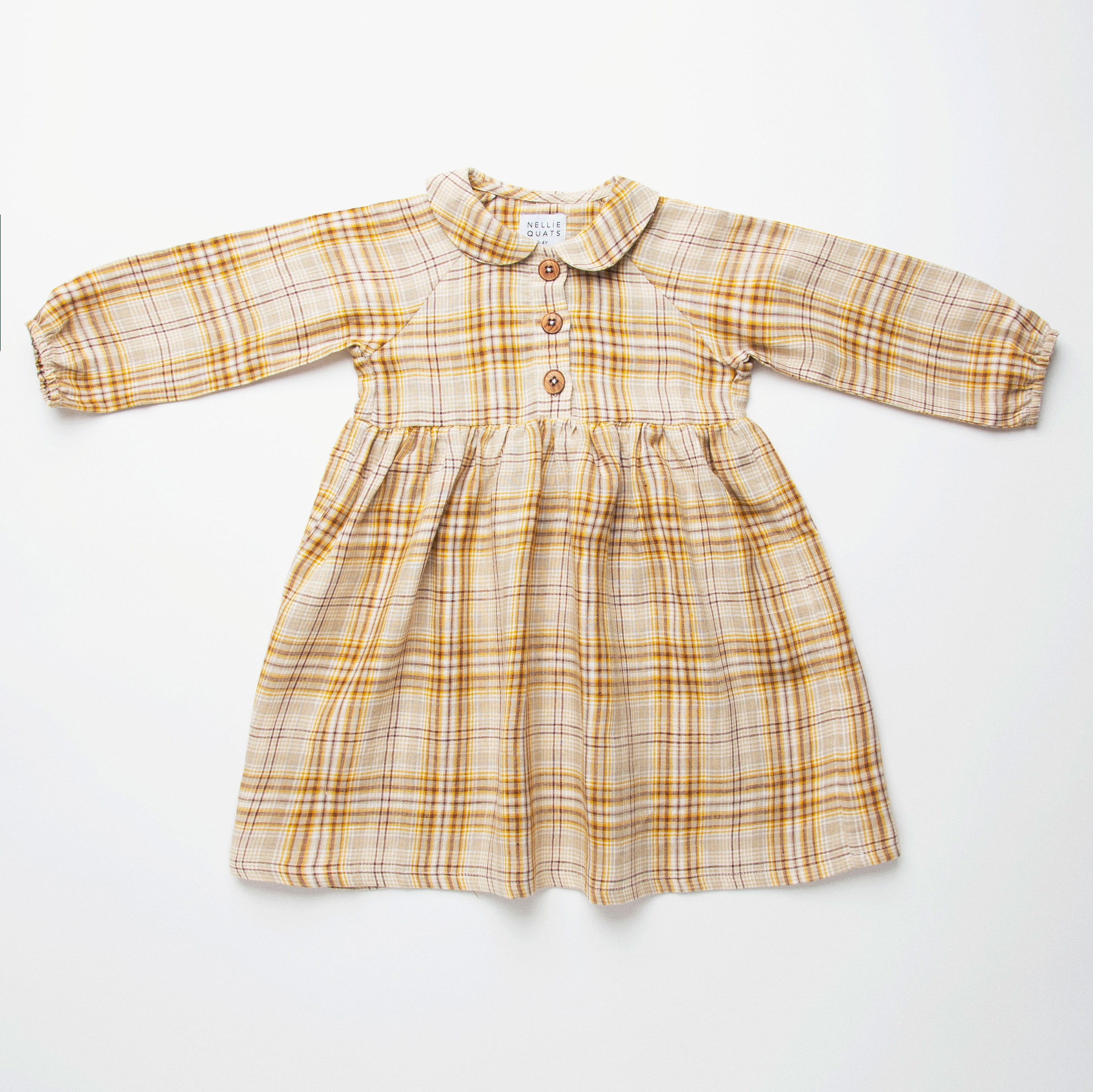 Long sleeve raglan dress with empire line, elasticated cuffs, Peter Pan collar and wooden button up front. Attached gathered skirt sits at a slightly longer length below the knee. Designed to be oversized for a stylish, comfortable fit. Made from a buttermilk plaid linen.