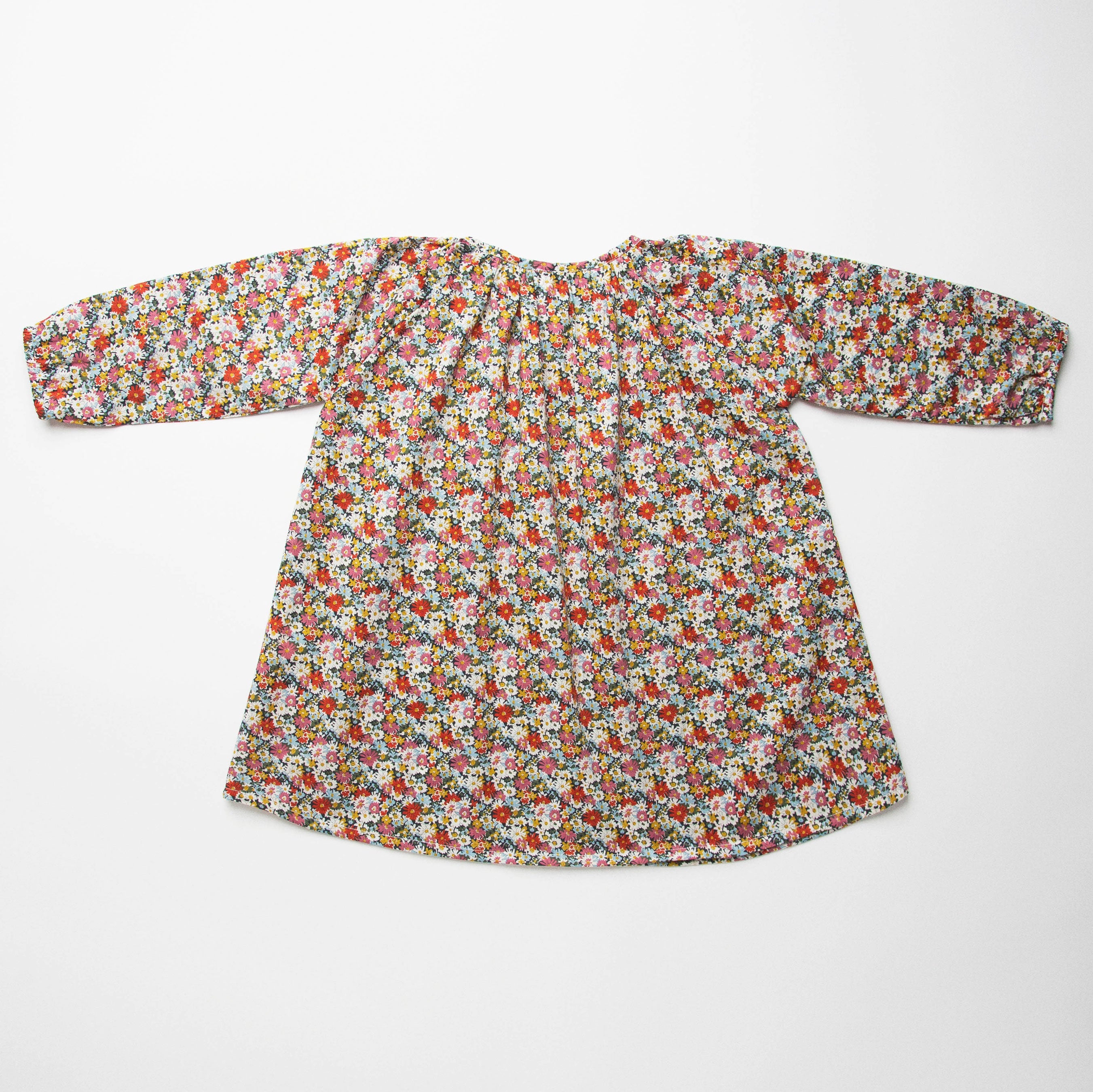Loose fit, raglan sleeve peasant dress, with puffed, long, full sleeves, elasticated cuffs and mother of pearl button up front. Neck line is gathered, to create an oversized style and comfortable fit. Two pockets sit at the front of the dress, perfect for storing treasures. Designed to sit above the knee and made from beautiful Libby Liberty print tana lawn cotton.