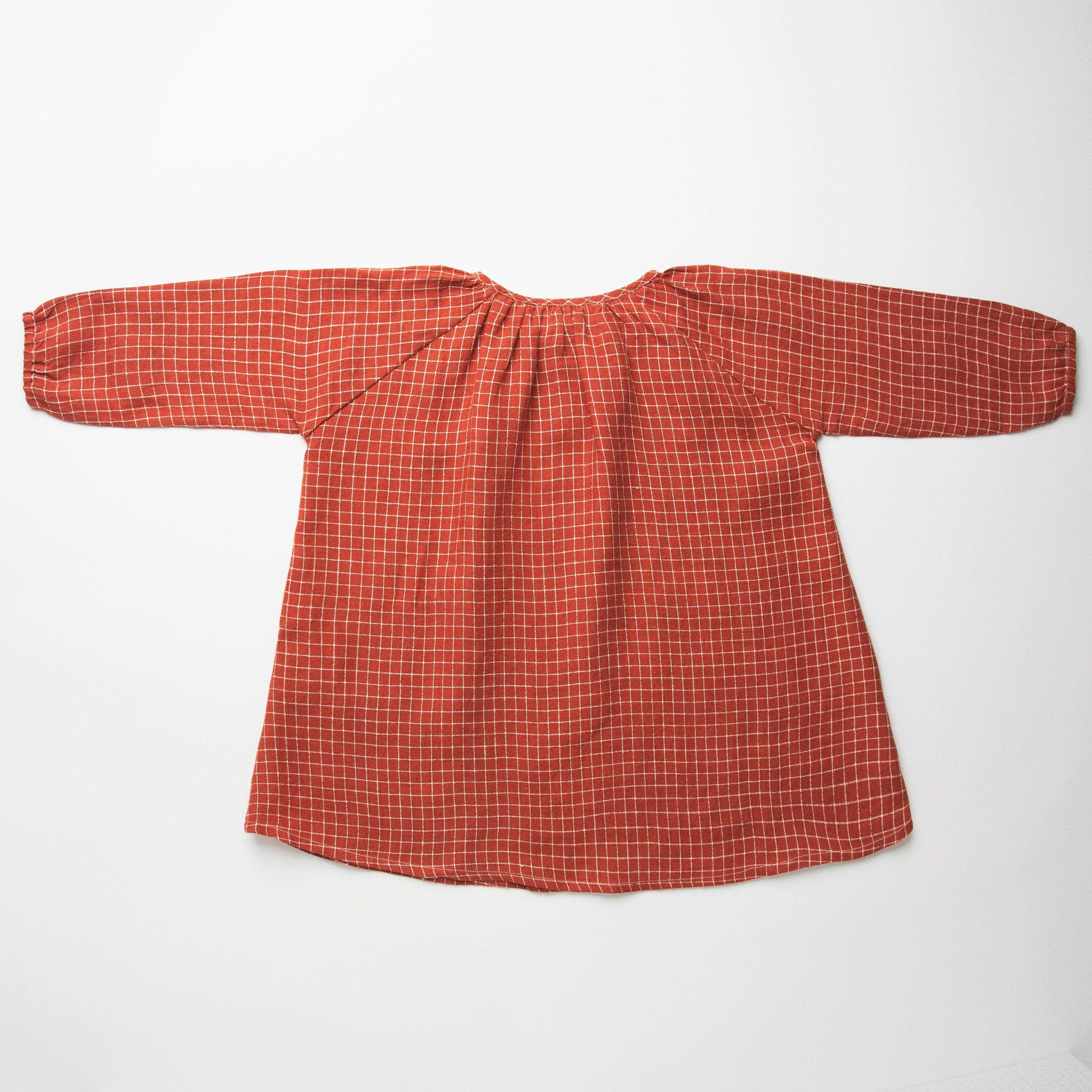 Loose fit, raglan sleeve peasant dress, with puffed, long, full sleeves, elasticated cuffs and mother of pearl button up front. Neck line is gathered, to create an oversized style and comfortable fit. Two pockets sit at the front of the dress, perfect for storing treasures. Designed to sit above the knee and made from super soft rust check linen.
