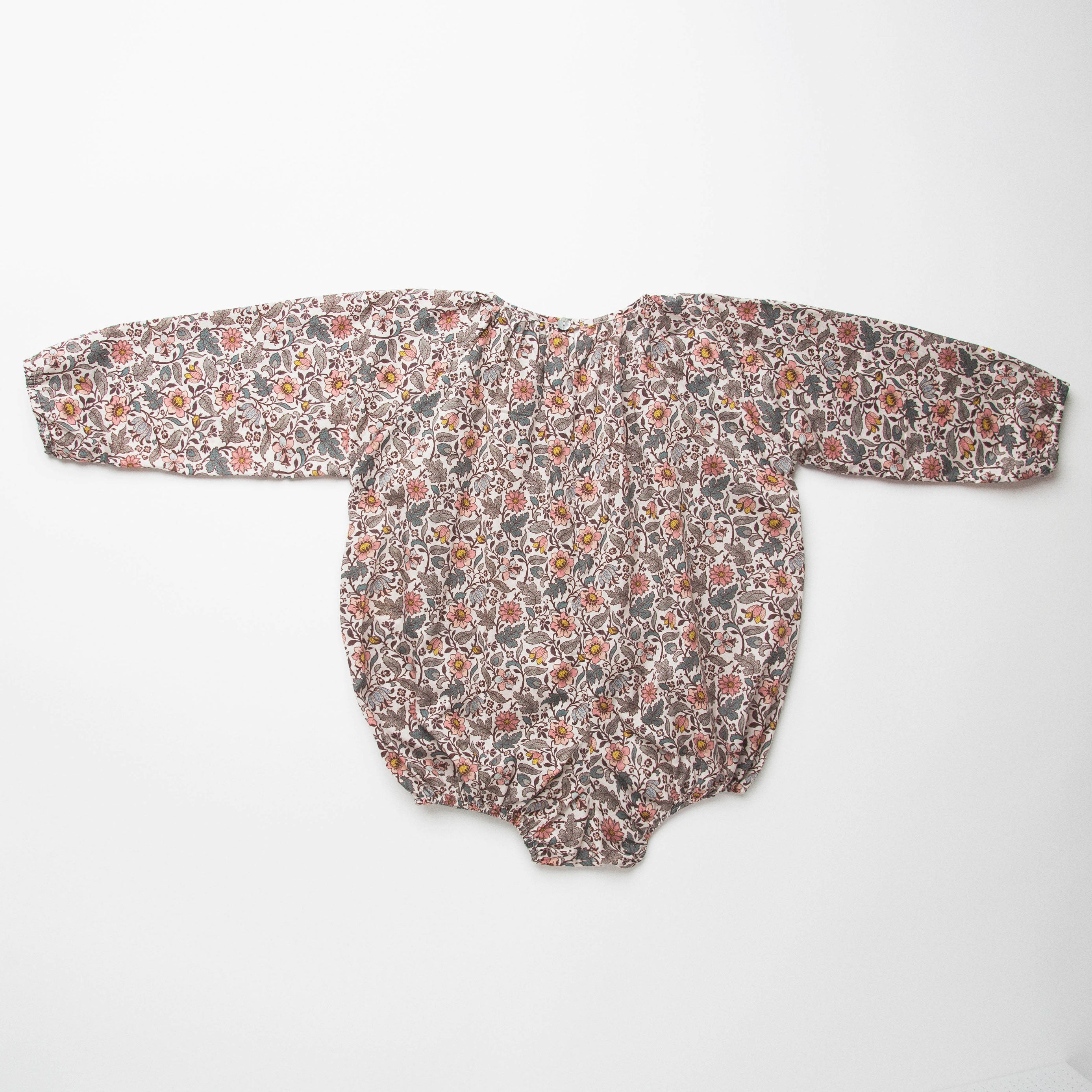 All in one romper, with long full elasticated sleeves and gathered neck to create a full, loose body shape. Closes at the back with single mother of pearl button, has elasticated leg holes and poppers for ease of opening. Designed to sit at the top of the thigh, perfect layered over tights in cooler weather and without in the summer. Made from Emery Walker Liberty print tana lawn cotton.