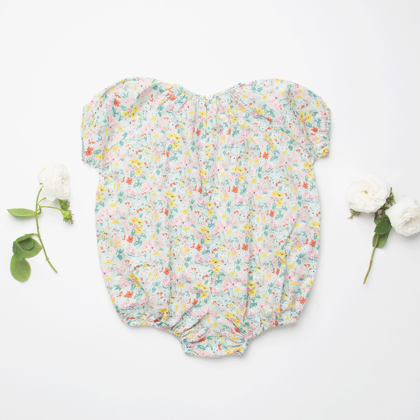 All in one romper, with short puffed elasticated sleeves and gathered neck to create a full, loose body shape. Closes at the back with single mother of pearl button, has elasticated leg holes and poppers for ease of opening. Designed to sit at the top of the thigh, perfect layered over tights in cooler weather and without in the summer. Made from beautiful California Bloom Liberty print tana lawn cotton.