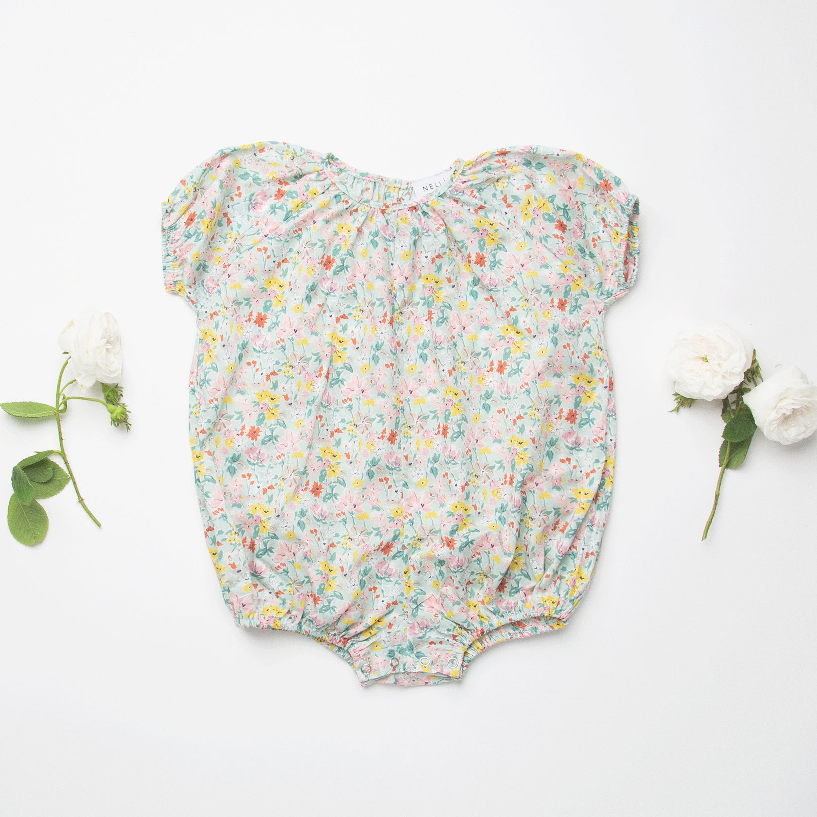 All in one romper, with short puffed elasticated sleeves and gathered neck to create a full, loose body shape. Closes at the back with single mother of pearl button, has elasticated leg holes and poppers for ease of opening. Designed to sit at the top of the thigh, perfect layered over tights in cooler weather and without in the summer. Made from beautiful California Bloom Liberty print tana lawn cotton.