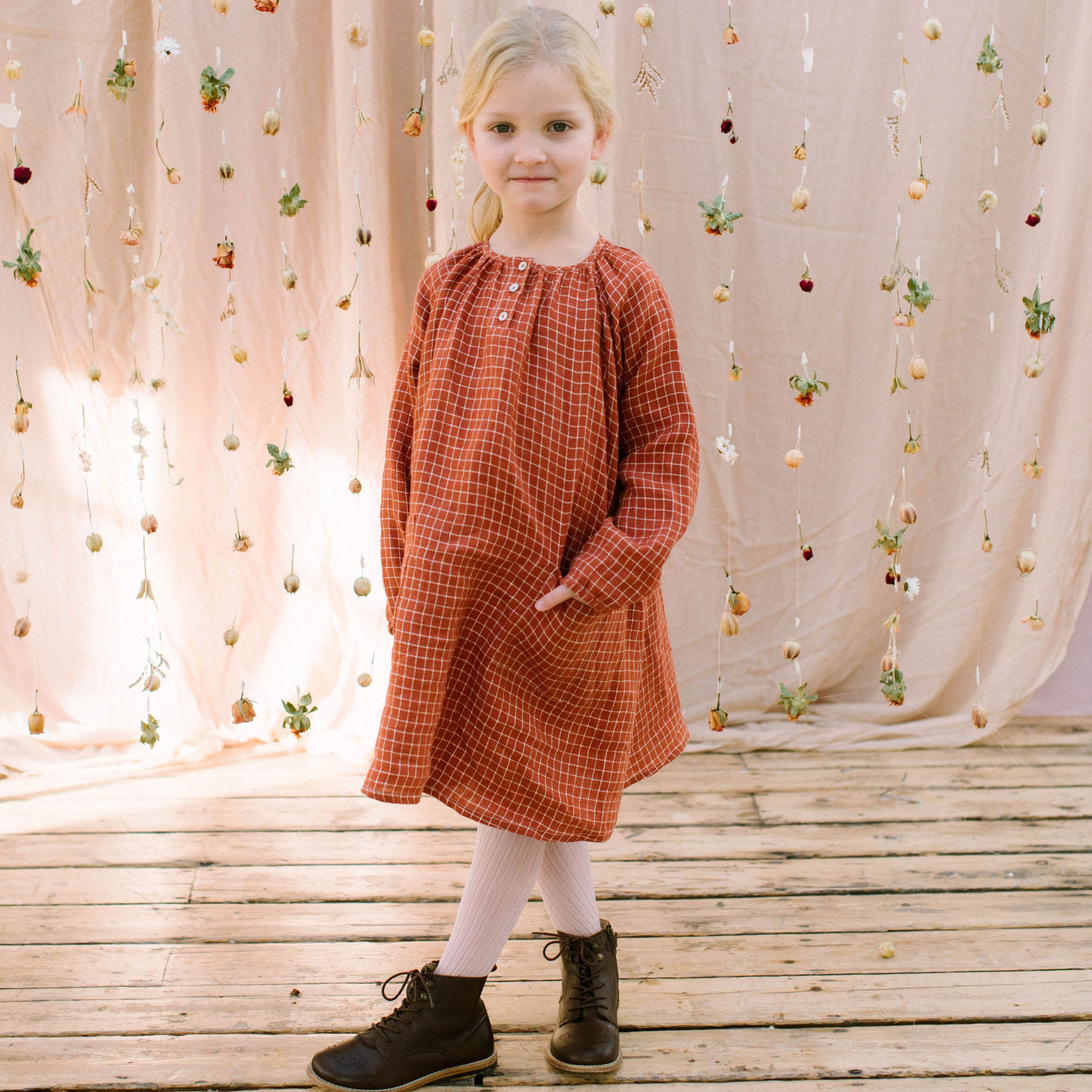Loose fit, raglan sleeve peasant dress, with puffed, long, full sleeves, elasticated cuffs and mother of pearl button up front. Neck line is gathered, to create an oversized style and comfortable fit. Two pockets sit at the front of the dress, perfect for storing treasures. Designed to sit above the knee and made from super soft rust check linen.
